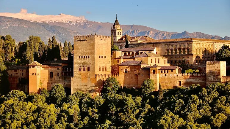 A castle with trees in front of it and mountains behind.