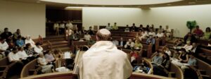 A priest is sitting in front of the audience.