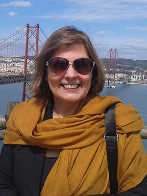 A woman in sunglasses and a scarf standing on top of a bridge.