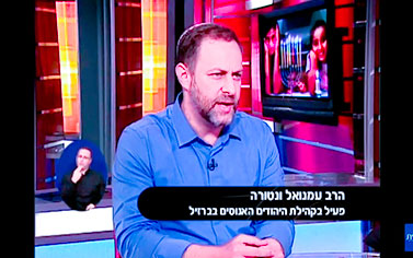 A man in blue shirt and black tie sitting on a tv set.