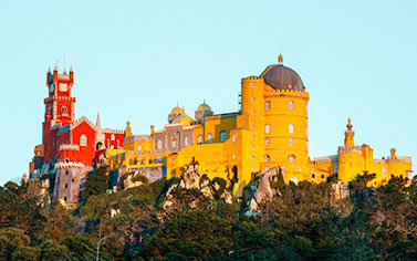 A yellow castle with many trees in the foreground