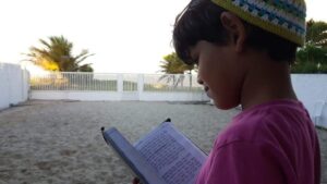 A boy is reading a book on the beach.