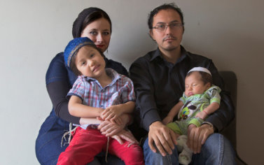 A family sitting on the couch with two babies.